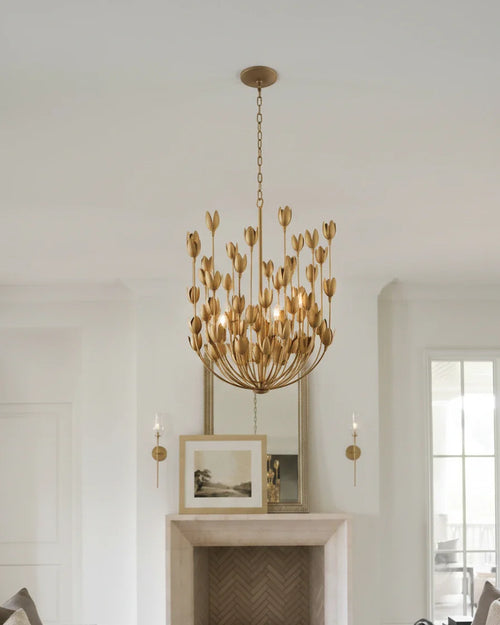 Aureline tiered flower chandelier in burnished gold, lit, hanging in a living room
