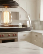 Industrial-style pendant light with a matte black iron frame and clear glass bowl shade lit over a marble kitchen island - detail 2