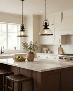 Industrial-style pendant light with a matte black iron frame and clear glass bowl shade lit over a marble kitchen island
