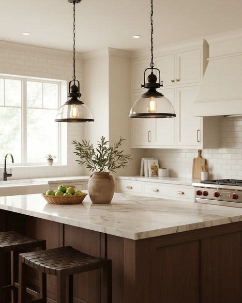 Industrial-style pendant light with a matte black iron frame and clear glass bowl shade lit over a marble kitchen island