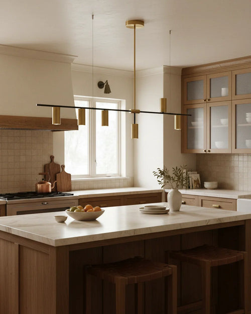 Modern linear island pendant with cylindrical gold and black shades on a horizontal bar, lit over a marble counter.