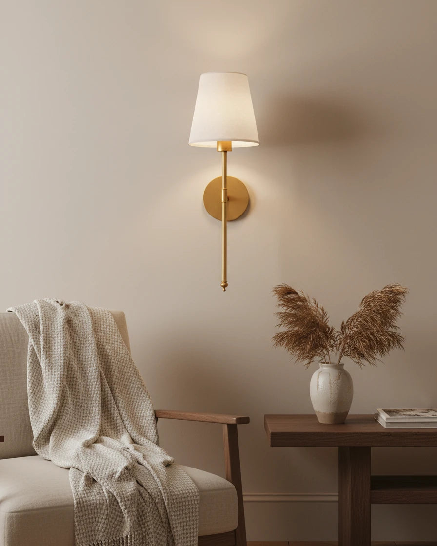 Gold wall sconce with a ribbed white fabric shade, lit in a warm bedroom setting - Black