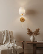 Gold wall sconce with a ribbed white fabric shade, lit in a warm bedroom setting - Black