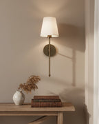 Gold wall sconce with a ribbed white fabric shade, lit in a warm bedroom setting - Black