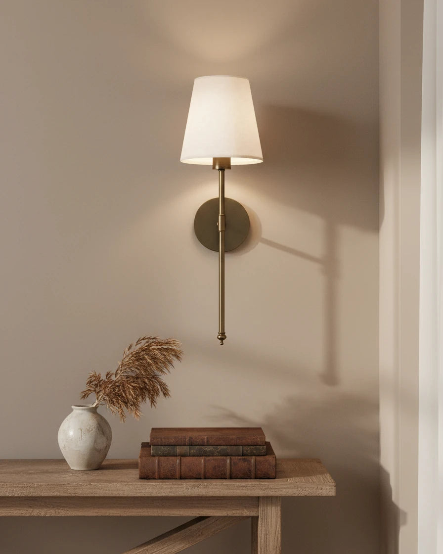 Gold wall sconce with a ribbed white fabric shade, lit in a warm bedroom setting - Black