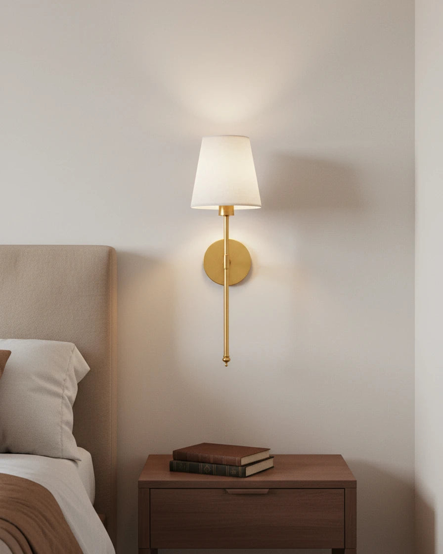Gold wall sconce with a ribbed white fabric shade, lit in a warm bedroom setting - Gold