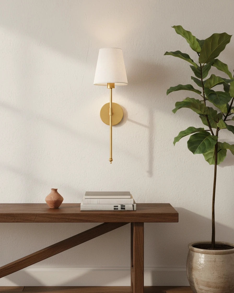Gold wall sconce with a ribbed white fabric shade, lit in a warm bedroom setting - Gold