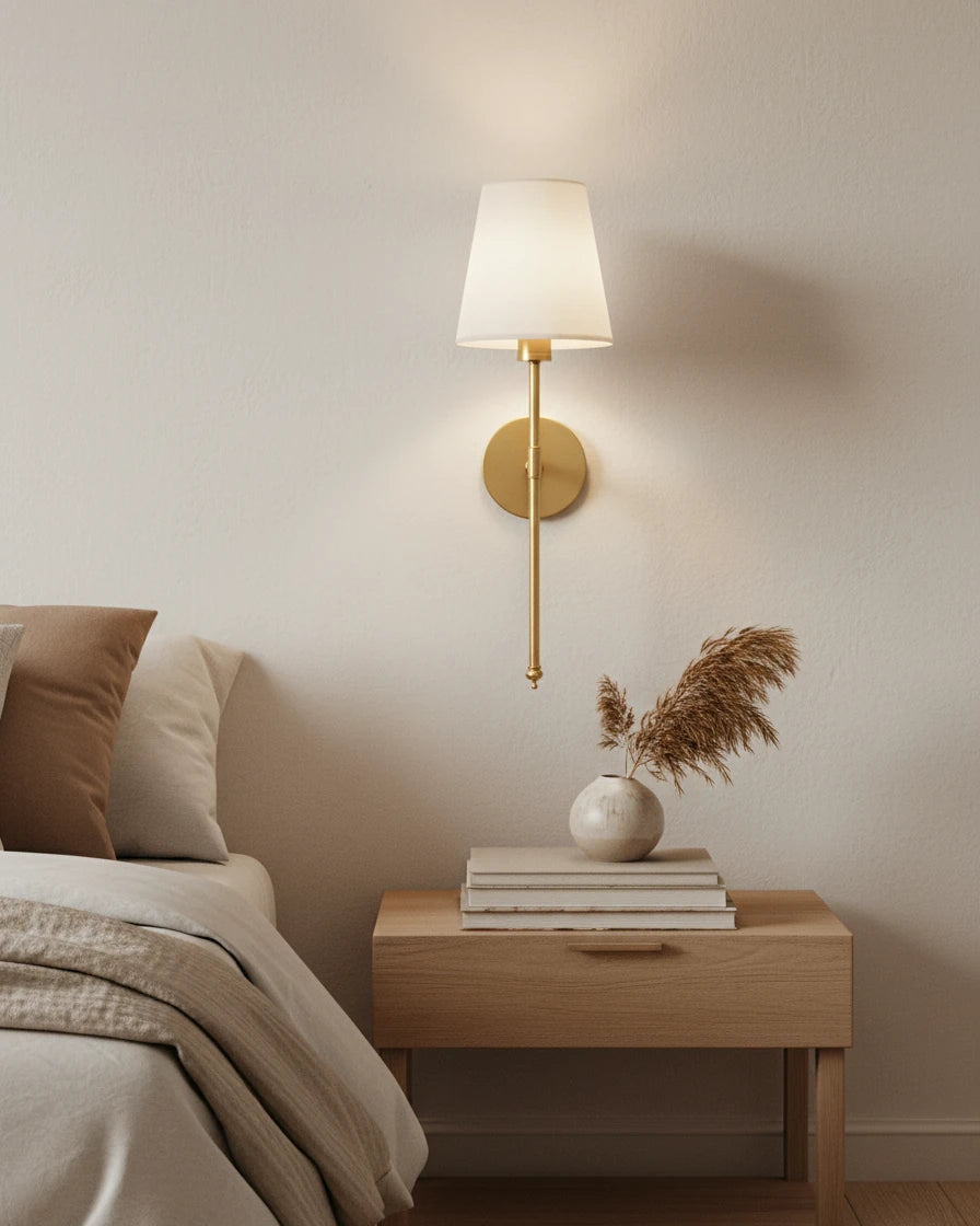 Gold wall sconce with a ribbed white fabric shade, lit in a warm bedroom setting - Silver
