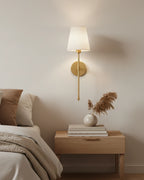 Gold wall sconce with a ribbed white fabric shade, lit in a warm bedroom setting - Silver