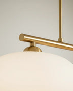 Linear 3-light pendant with gold finish and three spherical white glass shades, lit, in a kitchen setting - detail 1