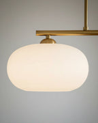 Linear 3-light pendant with gold finish and three spherical white glass shades, lit, in a kitchen setting - detail 2