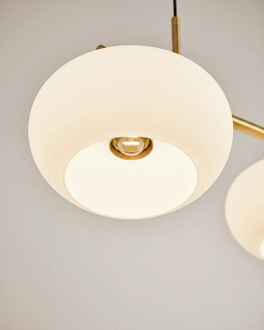 Linear 3-light pendant with gold finish and three spherical white glass shades, lit, in a kitchen setting - detail 4