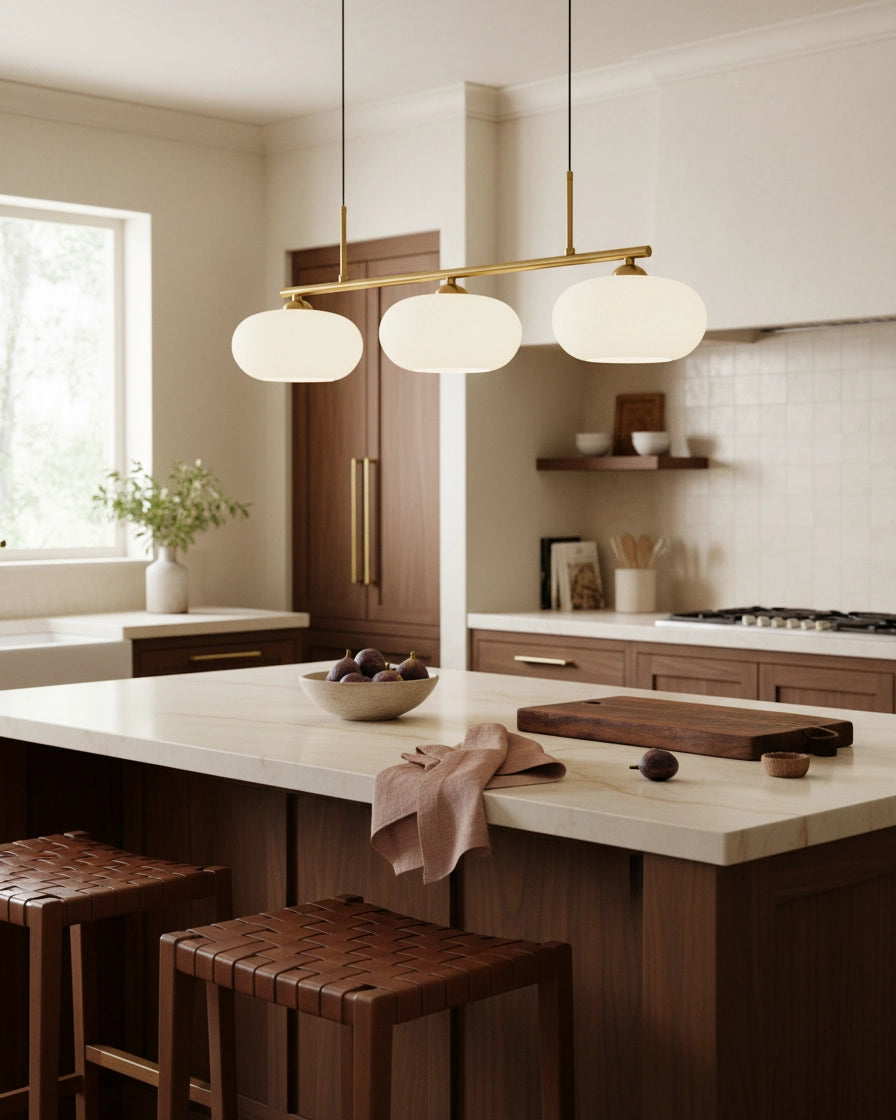 Linear 3-light pendant with gold finish and three spherical white glass shades, lit, in a kitchen setting - Gold