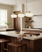 Linear 3-light pendant with gold finish and three spherical white glass shades, lit, in a kitchen setting - Gold