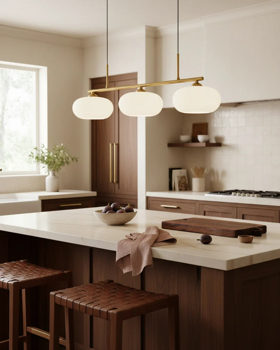 Linear 3-light pendant with gold finish and three spherical white glass shades, lit, in a kitchen setting - Gold