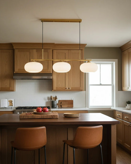 Linear 3-light pendant with gold finish and three spherical white glass shades, lit, in a kitchen setting