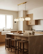 Linear 3-light pendant with gold finish and three spherical white glass shades, lit, in a kitchen setting - hero 2
