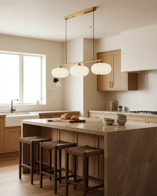 Linear 3-light pendant with gold finish and three spherical white glass shades, lit, in a kitchen setting - hero 2