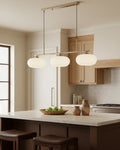 Linear 3-light pendant with gold finish and three spherical white glass shades, lit, in a kitchen setting - Nickel