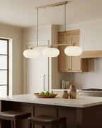 Linear 3-light pendant with gold finish and three spherical white glass shades, lit, in a kitchen setting - Nickel
